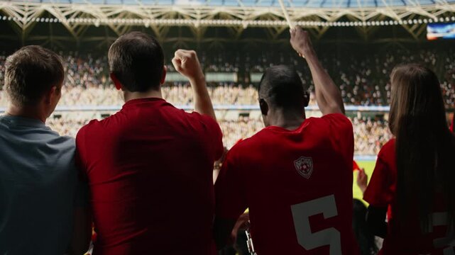 Wide back view of diverse cheering crowd in football stadium during live match, passionate supporters in red jerseys with scarves chanting from the supporter section terrace, football ultras.