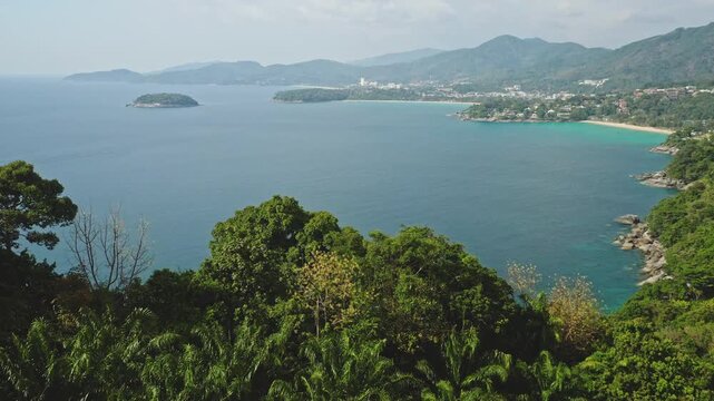 Wide aerial view showing the expansive blue ocean bay meeting lush green tropical coastline of Phuket, with popular Patong and Karon beaches nestled along the shore. Amazing drone flight panorama