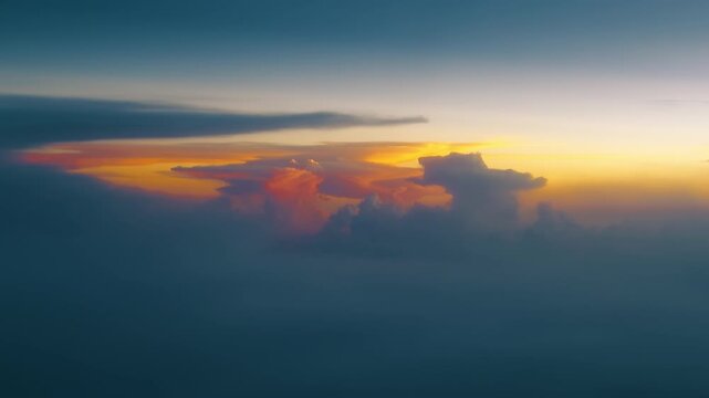 Stunning aerial view of dramatic sunset clouds illuminated with vibrant orange and pink hues floating above soft blue atmospheric haze. Golden hour light creates breathtaking contrast.