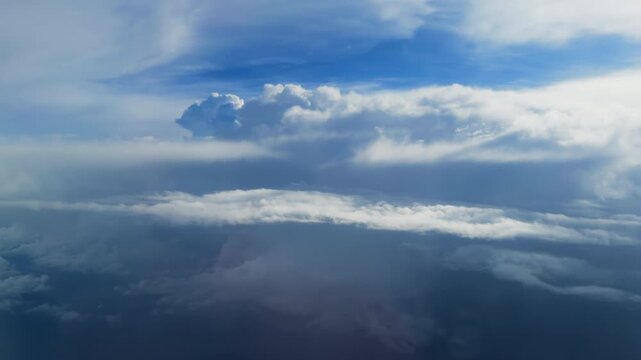 Stunning aerial perspective high above layered cloud formations with towering cumulonimbus clouds rising against deep blue sky. Multiple cloud layers create dramatic atmospheric depth and texture.