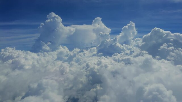 Aerial view of towering cumulus clouds with dramatic vertical formations reaching into clear blue sky. Fluffy white cloudscape creates majestic atmosphere with soft textures and natural beauty.