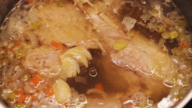 Turkey legs are simmering in a rich broth with vegetables. The soup gently boils. Slow cooking makes the meat tender and juicy while creating a clear, hearty broth. High quality 4k footage