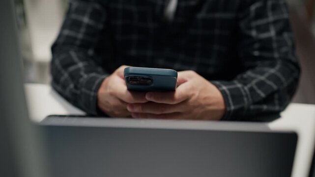 Close-up front view of a man software developer holding and text on smartphone device, working on computer network server security system at desk.