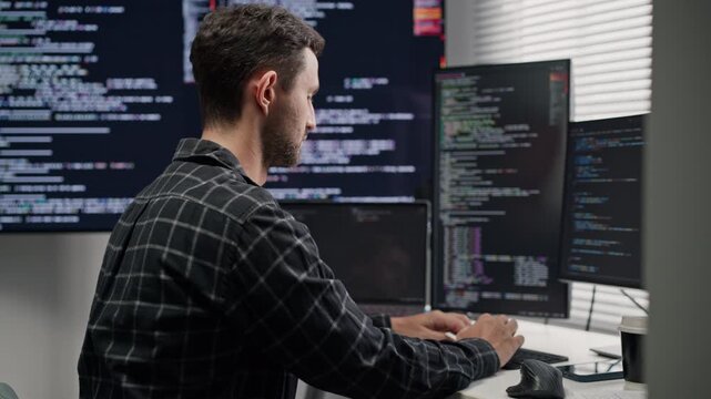 Concentrated man software developer looking at computer monitor, typing code for network server security system and programming at desk.