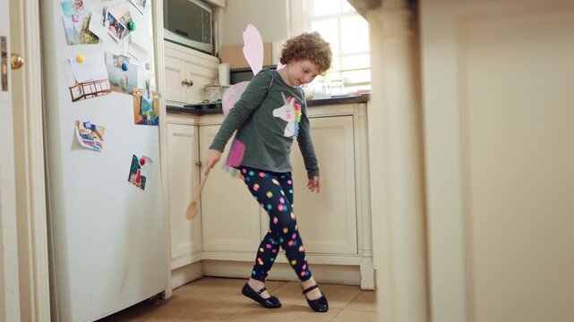 Costume, dancing and child with smile in kitchen, creative expression and playing for development. Childhood, spoon and girl with fantasy dress up for imagination growth, home and moving to music