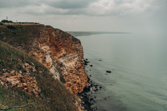 Dramatic limestone sea cliff above calm water under cloudy sky with wild grass coastal layers distant horizon natural travel landscape geology tourism and moody seaside atmosphere
