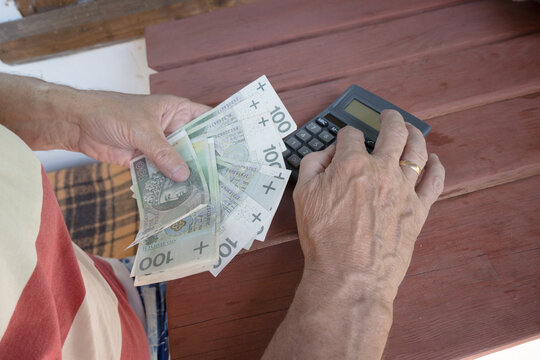 An elderly man counts expenses on a calculator, Polish money, hundred-zloty banknotes.
