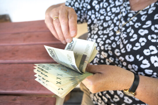 A senior citizen, a retiree, counts her pension to cover her bills. Polish 100-zloty banknotes.
