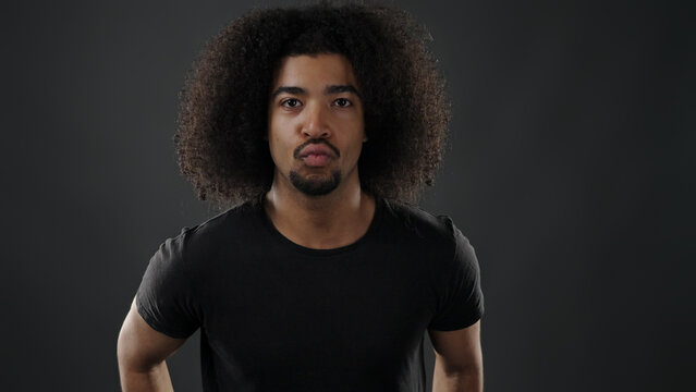 Young black man forming pouting lips expression on a dark background