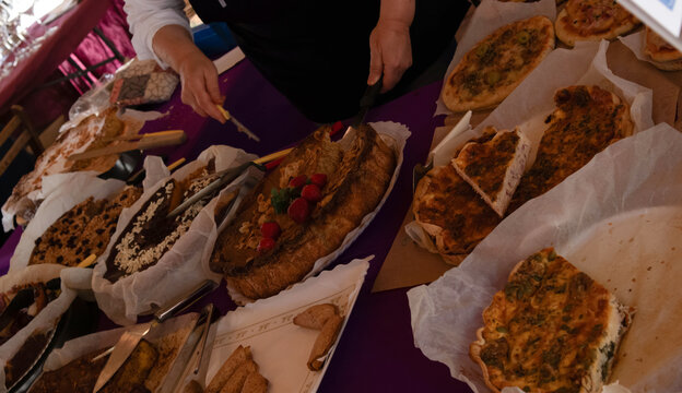 Person slices homemade savory tarts, pizzas, and a berry topped cake on a catering table during a casual event