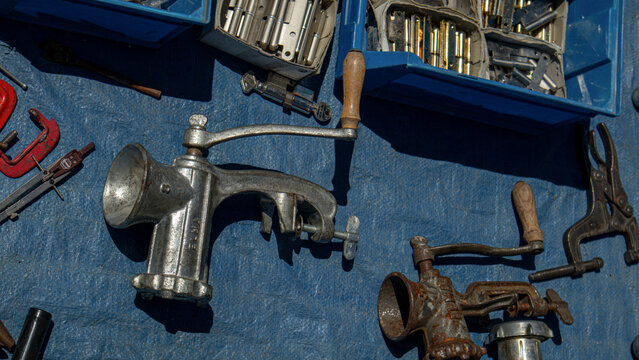 Polop, SPAIN - May 10, 2026.Vintage manual metal meat grinders and hardware tools arranged on a blue tarp at a local market during a sunny afternoon