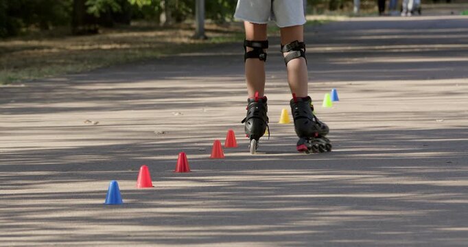 Girl skates past colorful cones during rollerblade training. Child keeps feet aligned following marked route with controlled movement on park pavement during lesson