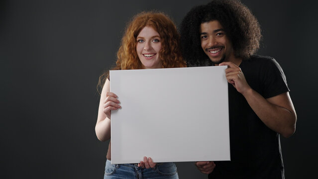 Smiling couple holding empty placard, showing togetherness and a diverse relationship