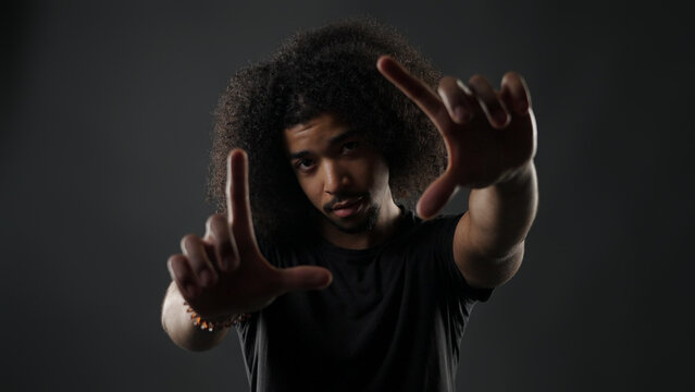 Man with afro hair framing hands on gray background, showing focus and creative choice