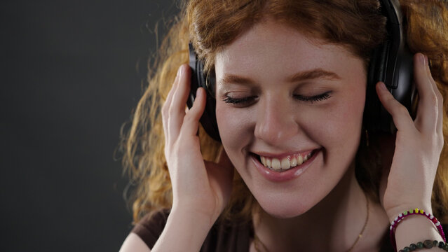 Young redhead woman closing her eyes and smiling while enjoying music through headphones