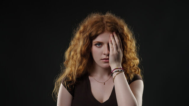 Young woman covering half of her face with her hand, revealing mystery or concealment