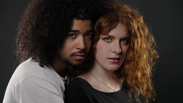 Young diverse couple embracing looking at camera against a dark background