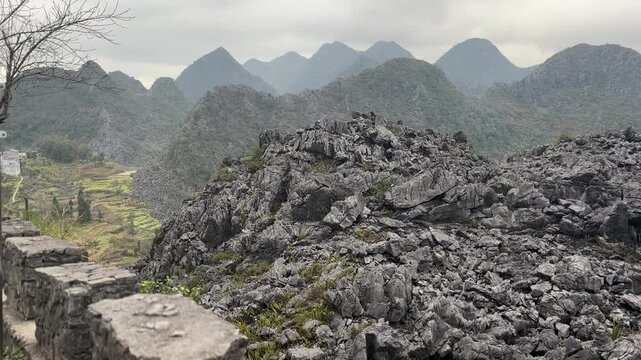 Rugged limestone rock field in Dong Van Karst Plateau Ha Giang Vietnam with jagged formations, rolling green mountain peaks and cloudy atmospheric landscape