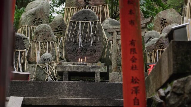 Kanji inscribed votive stones with straw offerings and lit candles framed by red torii gates at Fushimi Inari Kyoto