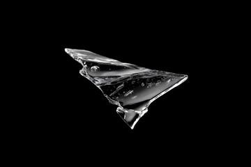 Naklejka premium Broken transparent glass shard isolated on a black background, with sharp cracked edges, glossy reflections, and dramatic high-contrast studio lighting.