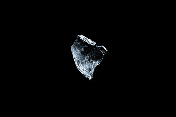 Naklejka premium Broken transparent glass shard isolated on a black background, with sharp cracked edges, glossy reflections, and dramatic high-contrast studio lighting.