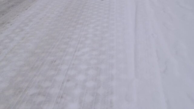 Outdoor handheld tracking shot moves forward over a ground layer of fresh white snow dusting textured diamond patterned concrete interlocking bricks by a sidewalk on a winter day.