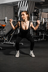 Fototapeta premium Beautiful woman in the gym with a barbell in a black tight tracksuit.