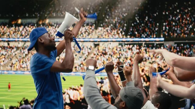 Passionate soccer supporter with megaphone leading stadium chant during football match in the crowded supporter section with supporter chants.