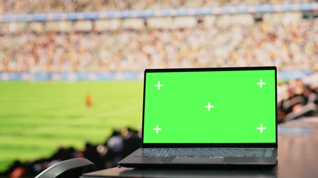 Green screen on laptop inside modern football stadium with green field, tribunes and soccer pitch for live match in the world tournament.