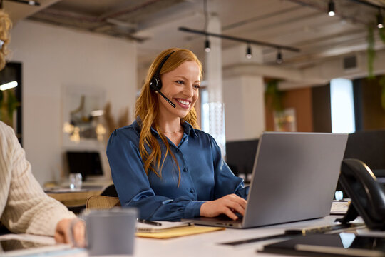 Happy customer service woman on call whiel workiong on laptop