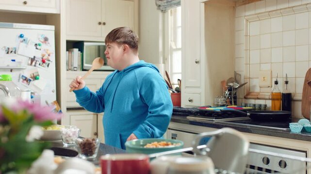 Man, dancing and singing with spoon in kitchen for playful cooking or fun meal prep in home. Karaoke, energy or male person with down syndrome or vibe for music, audio streaming or podcast in house