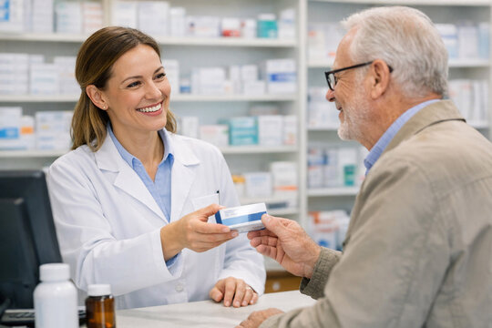 A pharmacist in a lab coat is helping an elderly man with his prescriptions at a pharmacy counter.