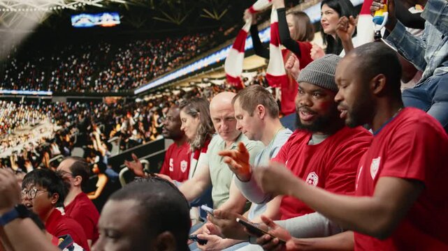 Football fans placing a risky bet ticket on in-play live gambling app, watching intense soccer match from the stadium stands.