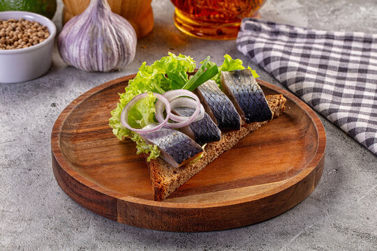 Traditional herring sandwich with red onion and lettuce on rye bread, served on a rustic wooden plate.