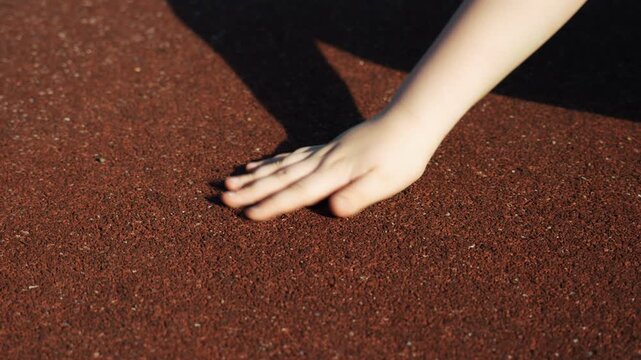 Children's pens touch the safe rubber crumb coating on the playground, in kindergarten, at school or at the stadium and show the class. Close-up.