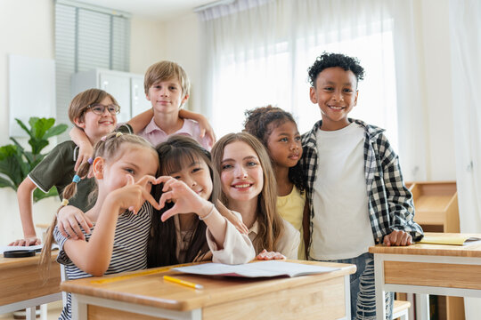 Diverse group of happy elementary students with teacher in classroom, Children and teacher smiling in class, Happy children showing heart gesture with teacher in classroom, Education concepts