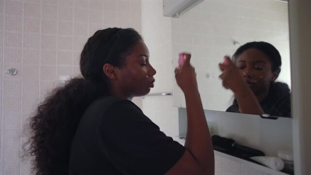 African American woman spraying facial mist then fanning face with hand to help product dry creating refreshing and natural finishing step in beauty routine at home