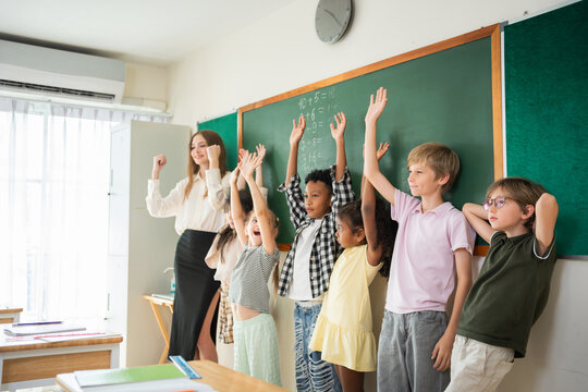 Diverse students raising hands in classroom with teacher, Enthusiastic pupils participating in school lesson with teacher, Inclusive education group raising hands in math class