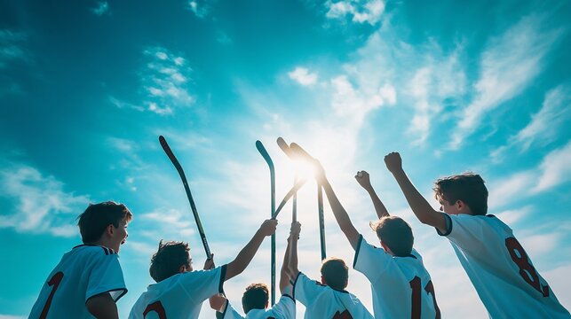 Young team of players holding their hockey sticks aloft in celebration after a victory with a bright blue sky teammates hugging and the excitement of the game palpable in the scene