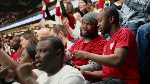 Football fans placing a risky bet ticket on in-play live gambling app, watching intense soccer match from the stadium stands, enthusiasts follow sports betting odds during important game.