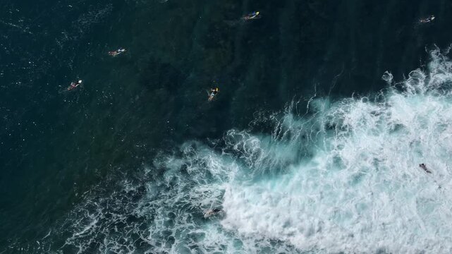 Surfers enjoying ocean waves, catching breaks and paddling back out in deep blue water of famous Bukit Peninsula surf spot in Bali, Indonesia. Active sports and recreation. Aerial view drone flight