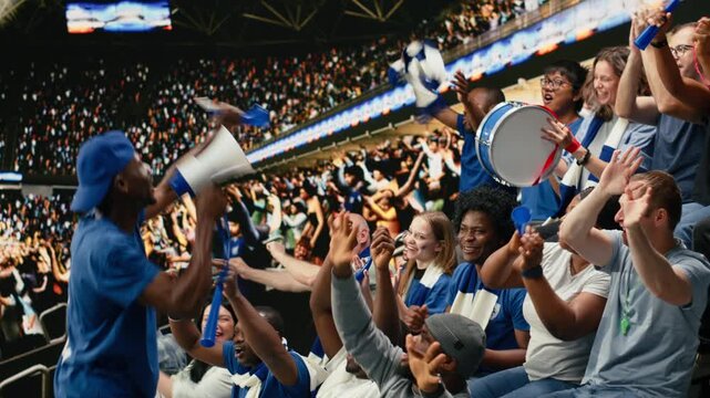 Energetic football fan with megaphone leading cheering supporters in stadium stands during intense soccer match, supporters in the fan zone cheering and creating powerful stadium noise.
