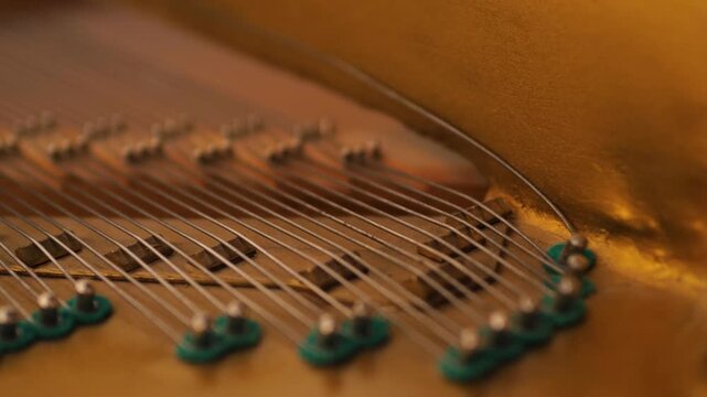 Macro shot of metal strings and tuning pins inside a vintage piano. Taut steel wires are fixed on the golden cast-iron frame of the musical instrument