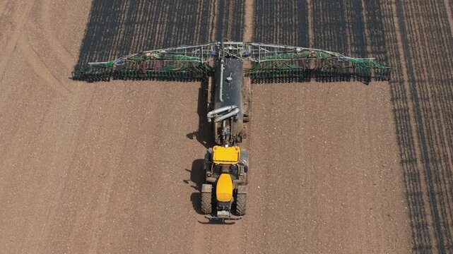 Tractor applying liquid organic manure fertilizer in agricultural field. Precision farming machinery improving soil fertility, crop yield, farm productivity. Sustainable agriculture, agribusiness