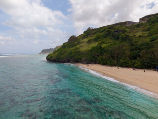 Obraz premium Aerial view of tropical white sand beach with turquoise coral reef ocean and lush green cliff hill