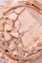 Fototapeta premium Broken pressed face powder compact with scattered beige powder and soft sparkle, delicate beauty product texture