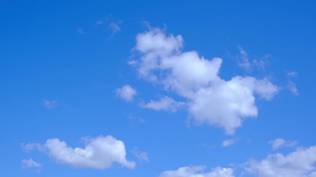 Bright, clear blue sky with scattered white clouds, including a large fluffy cumulus cloud and smaller cloud patches. Natural tranquil background. High quality 4K footage.