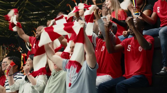 Excited football supporters celebrating with confetti in stadium stands, waving red scarves and cheering during live soccer match victory.