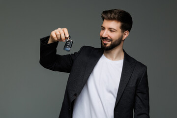 Young business man holding new car keys on gray background