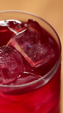 Ice cubes swirl in a glass of berry sparkling kombucha, top view. Iced fizzy drinks, and summer vibes.